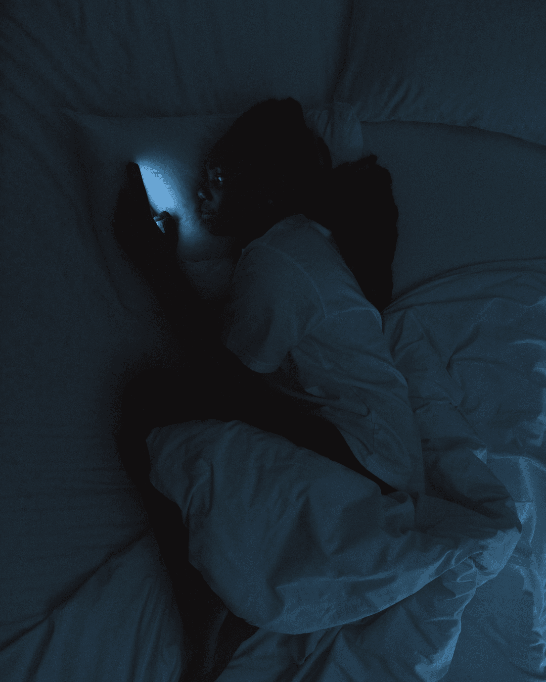 Person lying awake in the dark looking at a phone